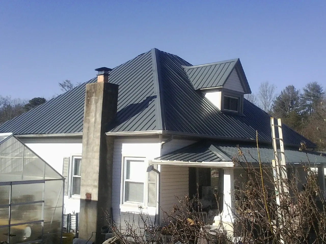Dark blue standing seam metal roof on a white farmhouse with dormer — Slate & Tile Roof Repair by Roofing Brothers in Malcom