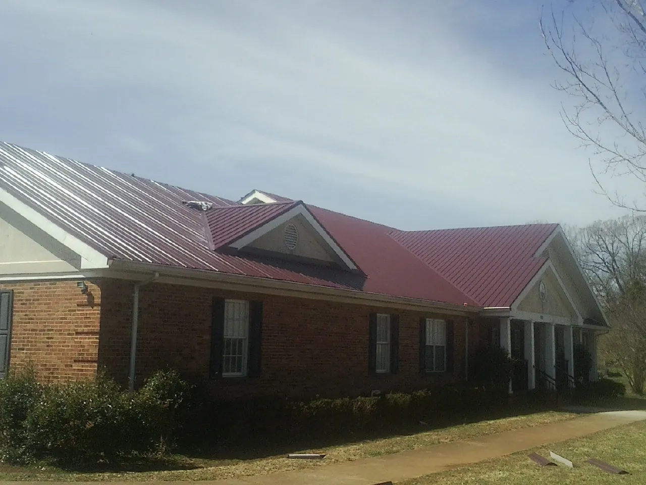 Red metal roof with gabled entries on a long brick building, from a Hail Damage Roof Repair job in Malcom