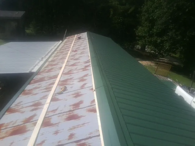 Old rusted panels beside newly installed green metal roofing — Wind Damage Roof Repair by Roofing Brothers in Malcom