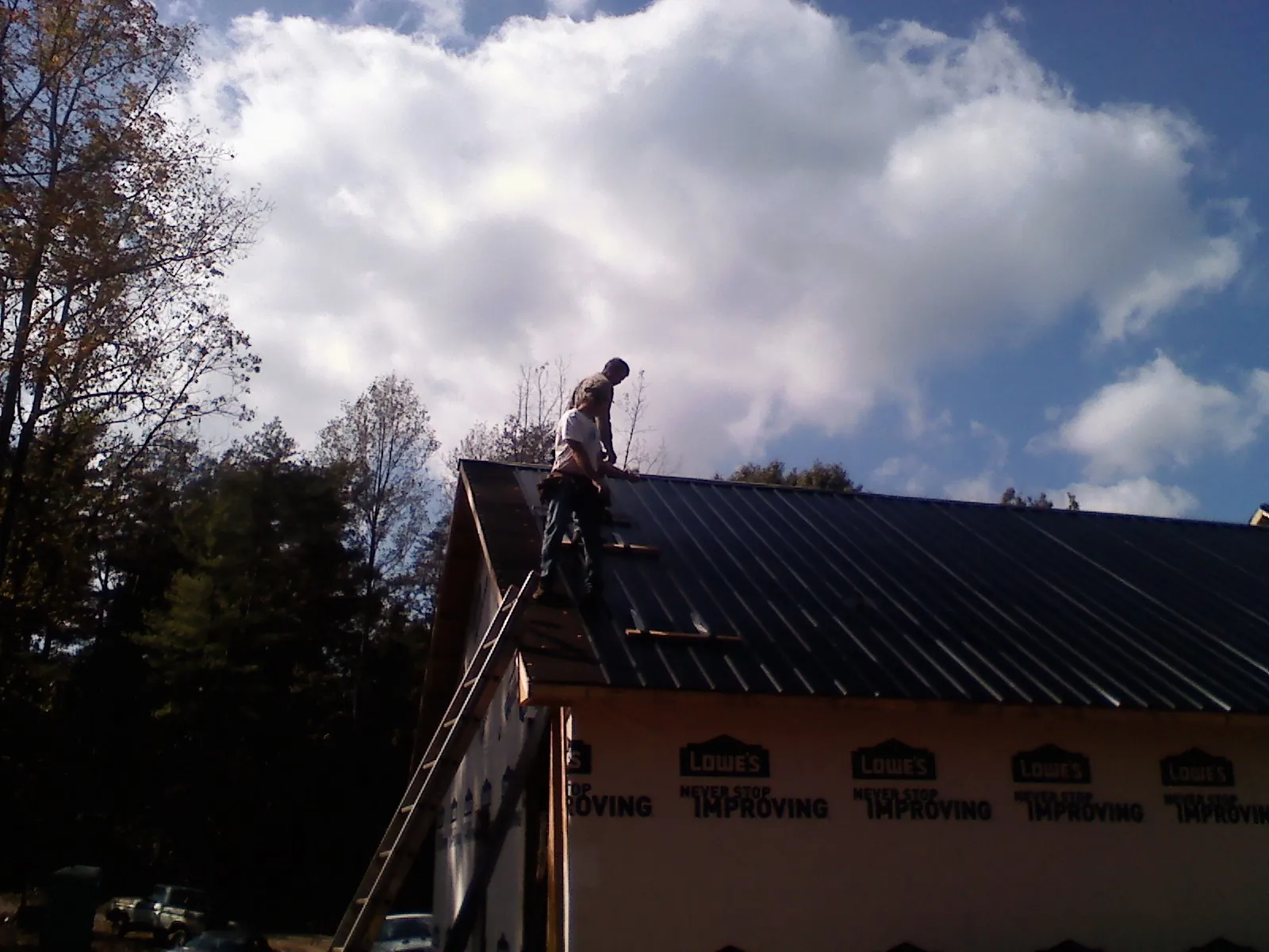 Roofer fastening dark metal panels high against a cloudy sky, from a Roof Inspection job in Malcom