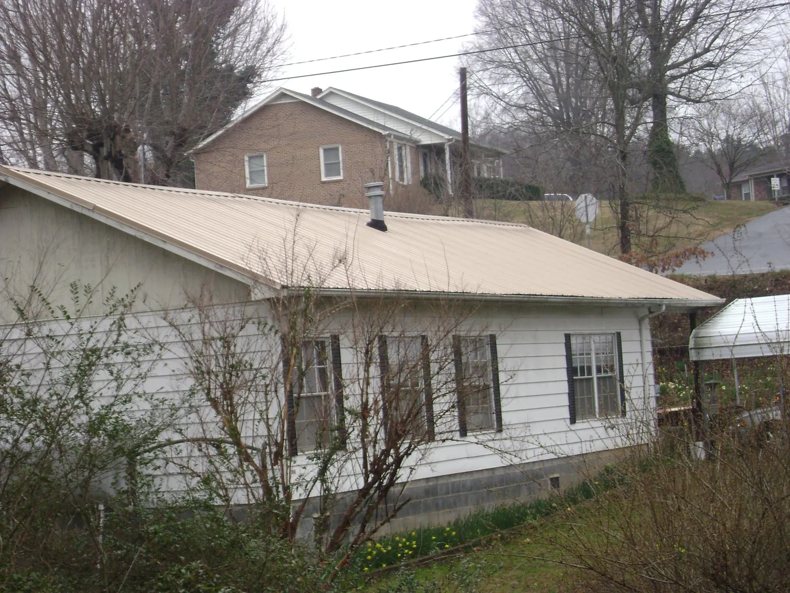 Tan metal roof on a white sided house set into a hillside — Commercial Roofing by Roofing Brothers in Malcom